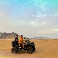 Dos personas en una cuatrimoto en el desierto, con cerros al fondo