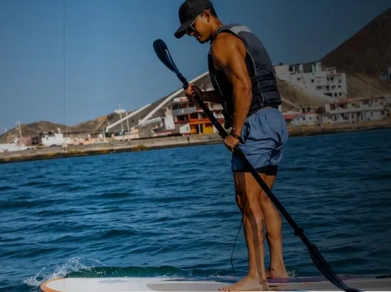 Hombre con chaleco salvavidas remando en paddle frente a la costa